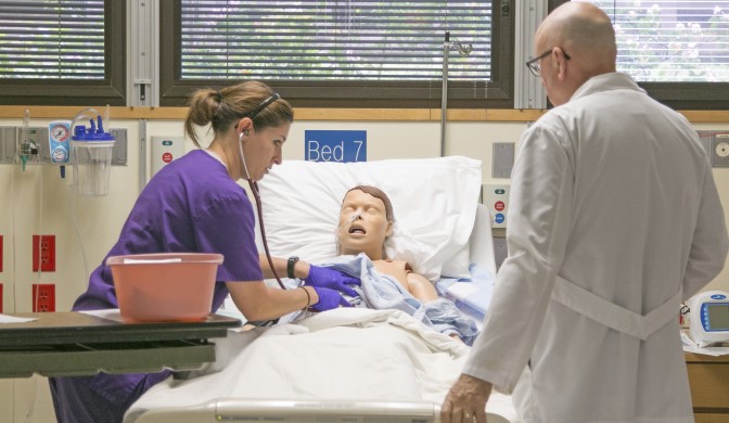 A nursing student learning patient care with a simulated patient and professor.