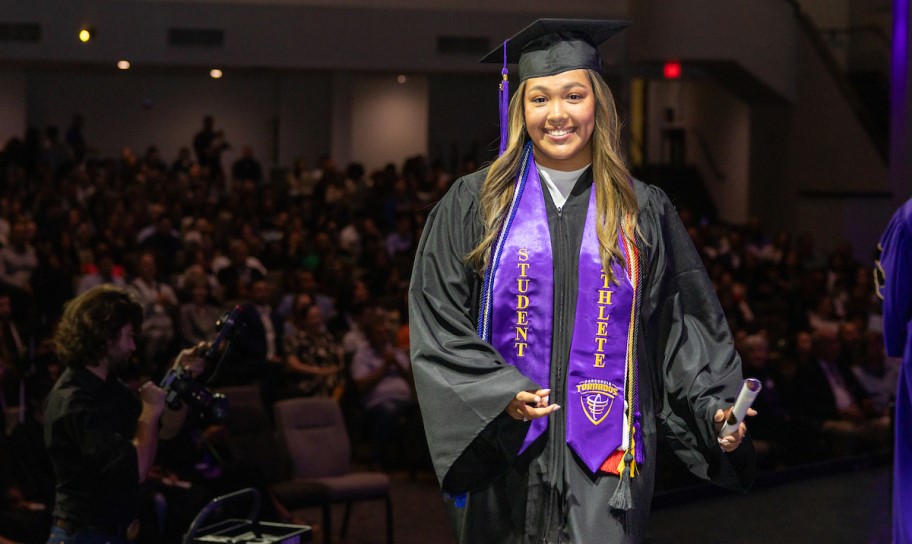 Graduating student-athlete wearing a stole or holding a diploma, ideally in an athletics venue